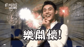a man is smiling in front of a fireworks display with chinese writing on it .