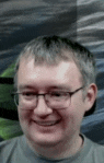 a man wearing glasses and a gray shirt is smiling for the camera .