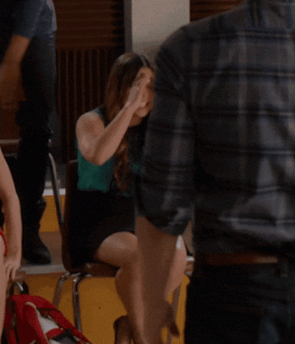 a cheerleader wearing a hs uniform sits next to another girl