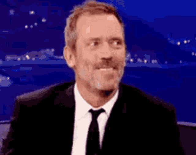 a man in a suit and tie is smiling with a blue background behind him