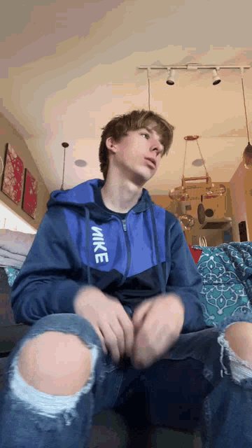 a young man wearing a blue nike jacket and ripped jeans