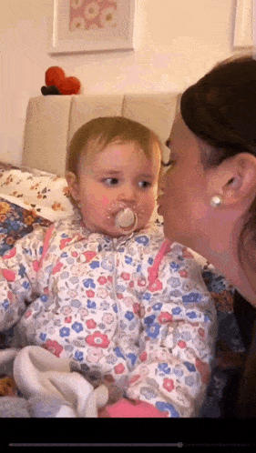 a woman is kissing a baby with a pacifier in its mouth