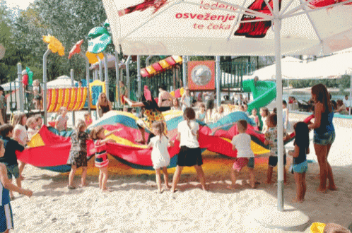 a group of children are playing in the sand under an umbrella that says ' osvezenje te ceka ' on it