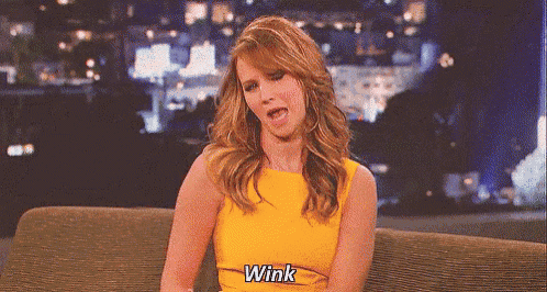 a woman in a yellow dress is sitting on a couch and making a funny face .