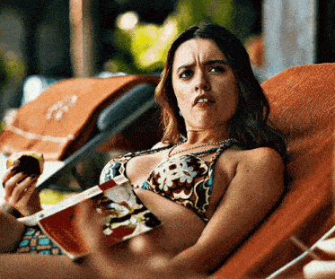 a woman in a bikini is reading a book while eating a donut