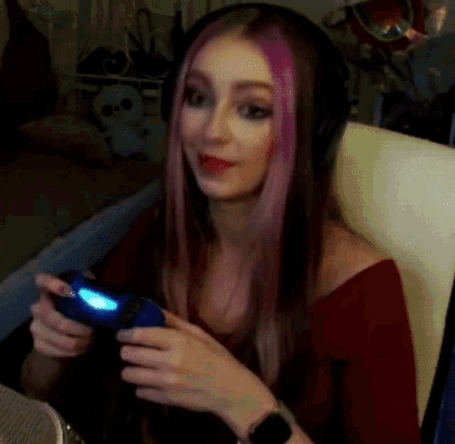 a woman with pink hair and headphones is holding a video game controller .