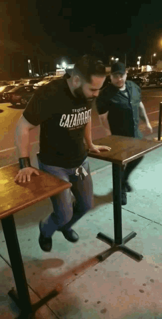 a man wearing a tequila cazador t-shirt stands next to another man