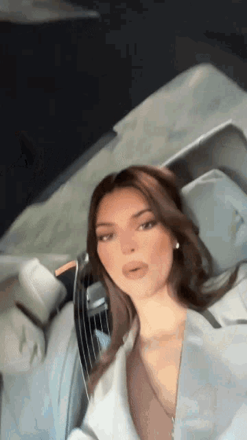 a woman is laying on a bed wearing a white shirt and taking a selfie .