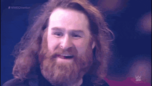 a man with long hair and a beard is making a funny face on a wrestling show .
