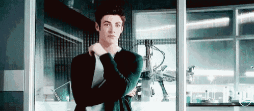 a young man is standing in a room with his arms crossed and a robot in the background .