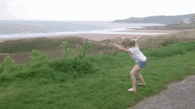 a little girl is standing in the grass near the ocean