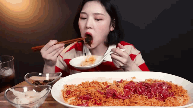 a woman eating noodles with chopsticks and a spoon