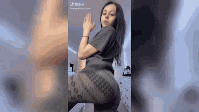 a woman in a gray shirt and leggings is sitting on a bed and dancing .