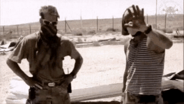 two men in military uniforms are standing next to each other on the beach .