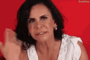 a woman with dark hair is wearing a white shirt and earrings and making a funny face .