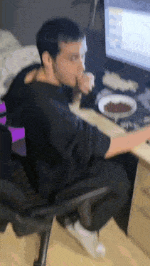 a man is sitting at a desk with a bowl of cereal in front of him .