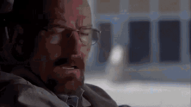 a man with glasses and a beard is sitting in a chair .