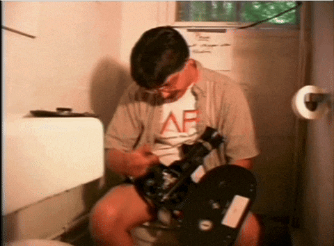 a man is sitting on a toilet with a camera and a shirt that says af
