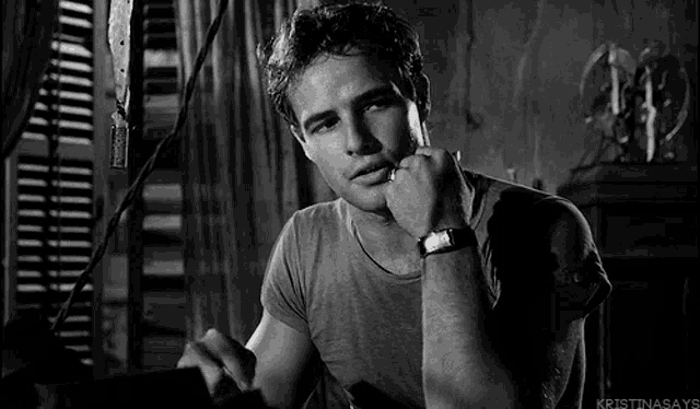 a black and white photo of a man wearing a watch with his hand on his chin .