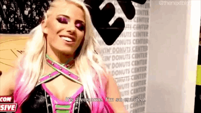 a female wrestler is standing in front of a wall that says donuts center and smiling .