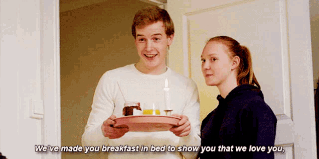 a man is holding a tray with candles on it next to a girl who says we 've made you breakfast