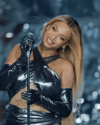 a woman in a black dress is singing into a microphone and smiling