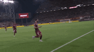 a man in a maroon shirt is dancing on a soccer field at night