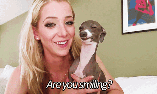 a woman is holding a small dog and smiling with the words are you smiling below her