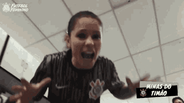 a woman in a black nike shirt is screaming in a room with minas do timão written on the bottom