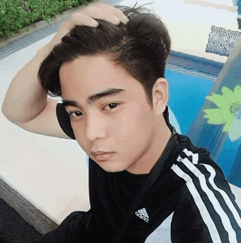 a young man in a black adidas shirt holds his hair