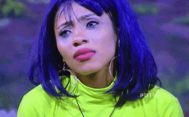 a woman with blue hair is wearing a neon green shirt and hoop earrings