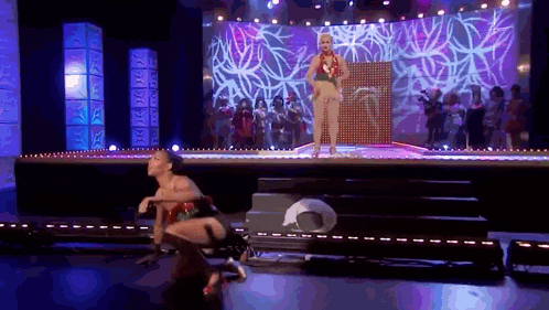a woman in a bikini is dancing on a stage while a group of people watch .