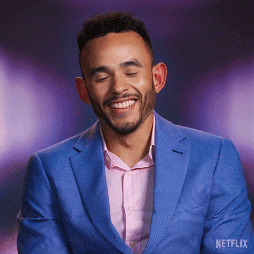 a man wearing a blue suit and a pink shirt is smiling with a netflix logo behind him