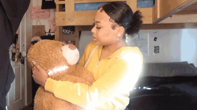 a woman in a yellow hoodie holds a teddy bear in her arms