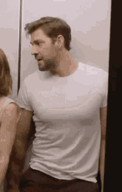 a man in a white t-shirt is standing next to a woman in a bathroom .