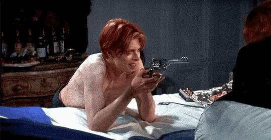 a shirtless man laying on a bed holding a revolver