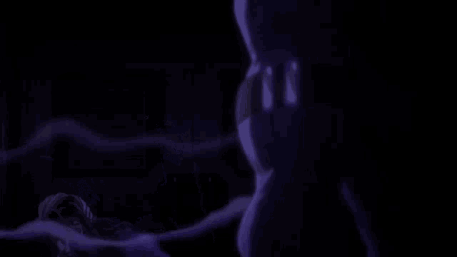 a man in a purple shirt is standing next to a stuffed animal in a dark room