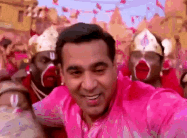 a man in a pink shirt is smiling in front of a crowd of people