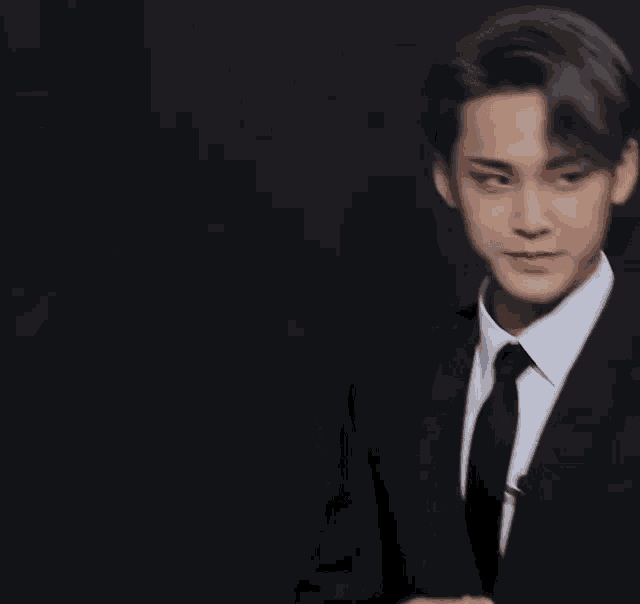 a young man in a suit and tie is standing in front of a black background .