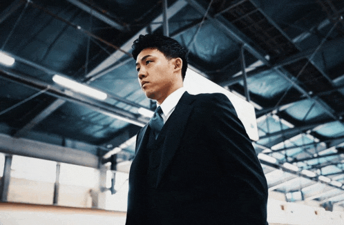a man in a black suit and white shirt stands in a dark room