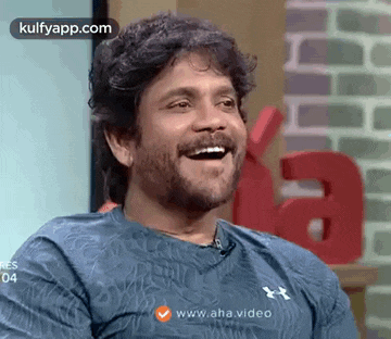 a man with a beard and mustache is laughing while wearing a blue shirt .