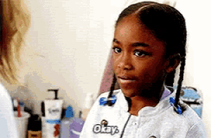 a little girl with braids is wearing a white shirt that says okay