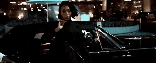a woman is standing next to a black car at night .