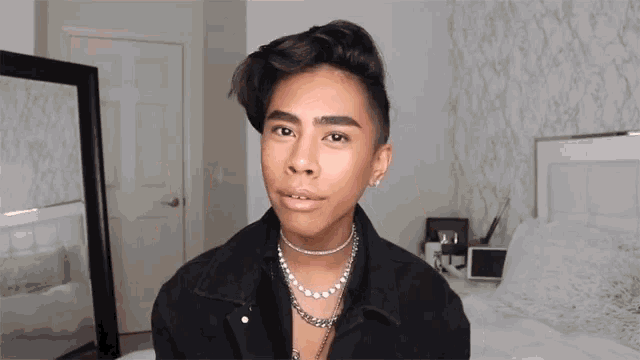 a young man wearing a black jacket and a pearl necklace