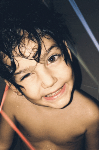 a young boy without a shirt is smiling and looking up at the camera