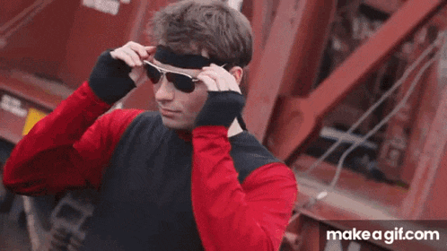 a man wearing sunglasses and a headband is standing in front of a red train .