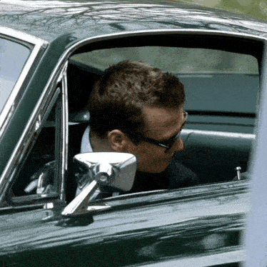a man in a suit and sunglasses is sitting in a car