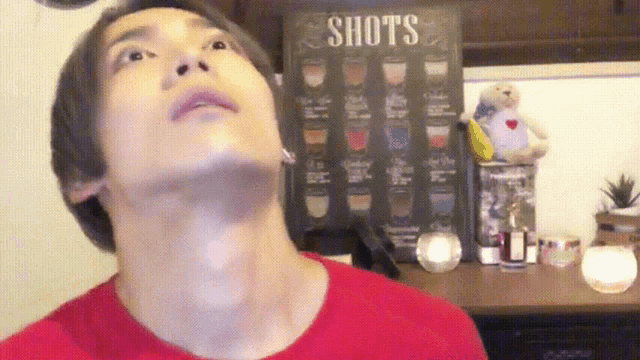 a man in a red shirt is looking up at a sign that says shots