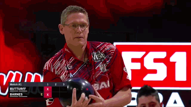 a man in a red shirt is holding a bowling ball in front of a sign that says fs1