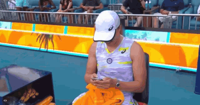 a woman wearing a white asics hat sits on a chair looking at her cell phone